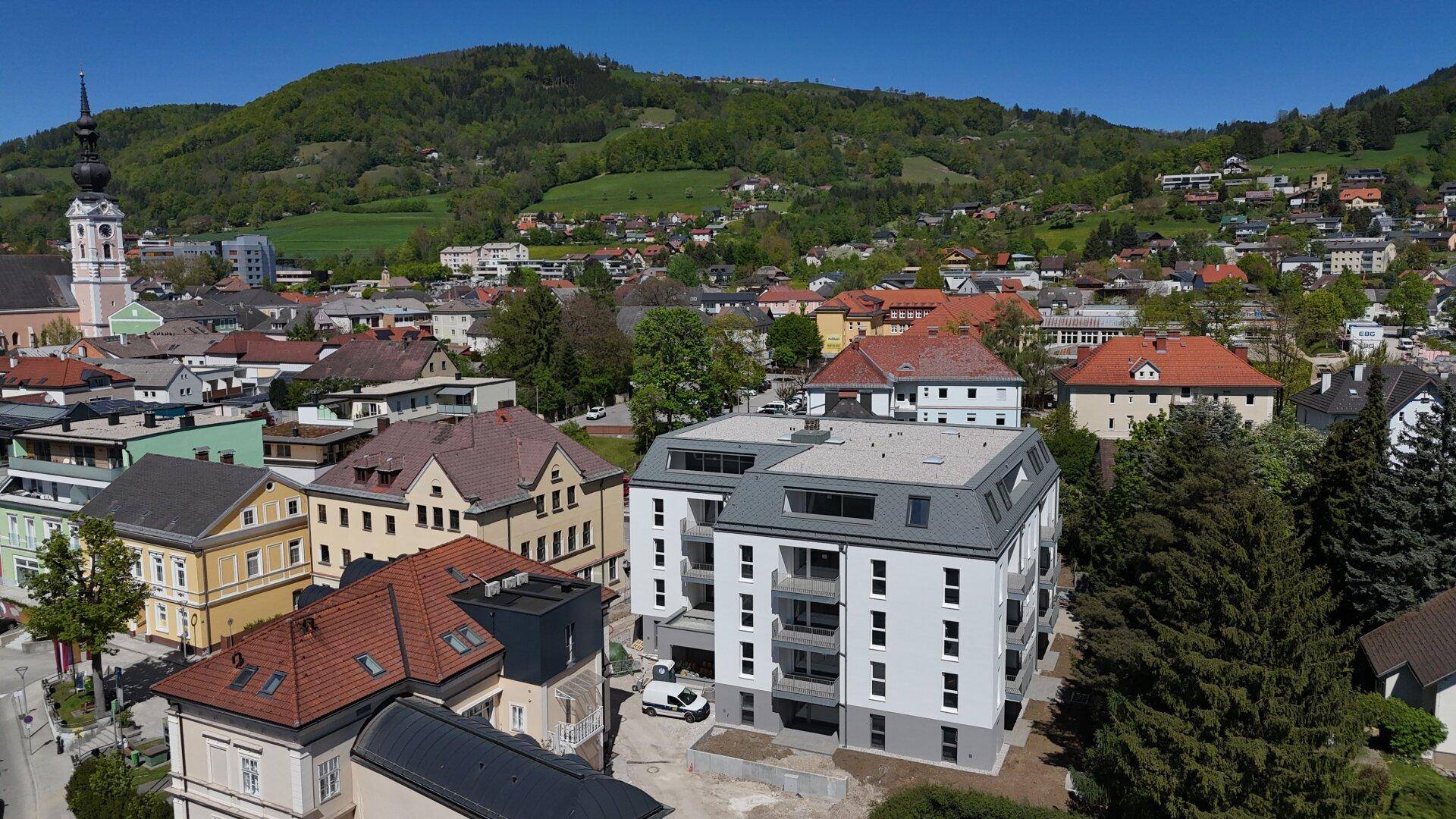 Luftaufnahme eines modernen Wohngebäudes in einer städtischen Umgebung mit grünen Hügeln im Hintergrund.