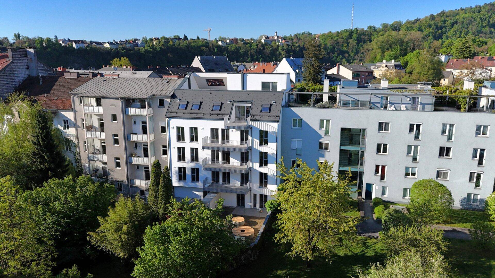 Panoramablick auf die moderne Wohnanlage mit umliegender grüner Landschaft und Hügeln im Hintergrund.