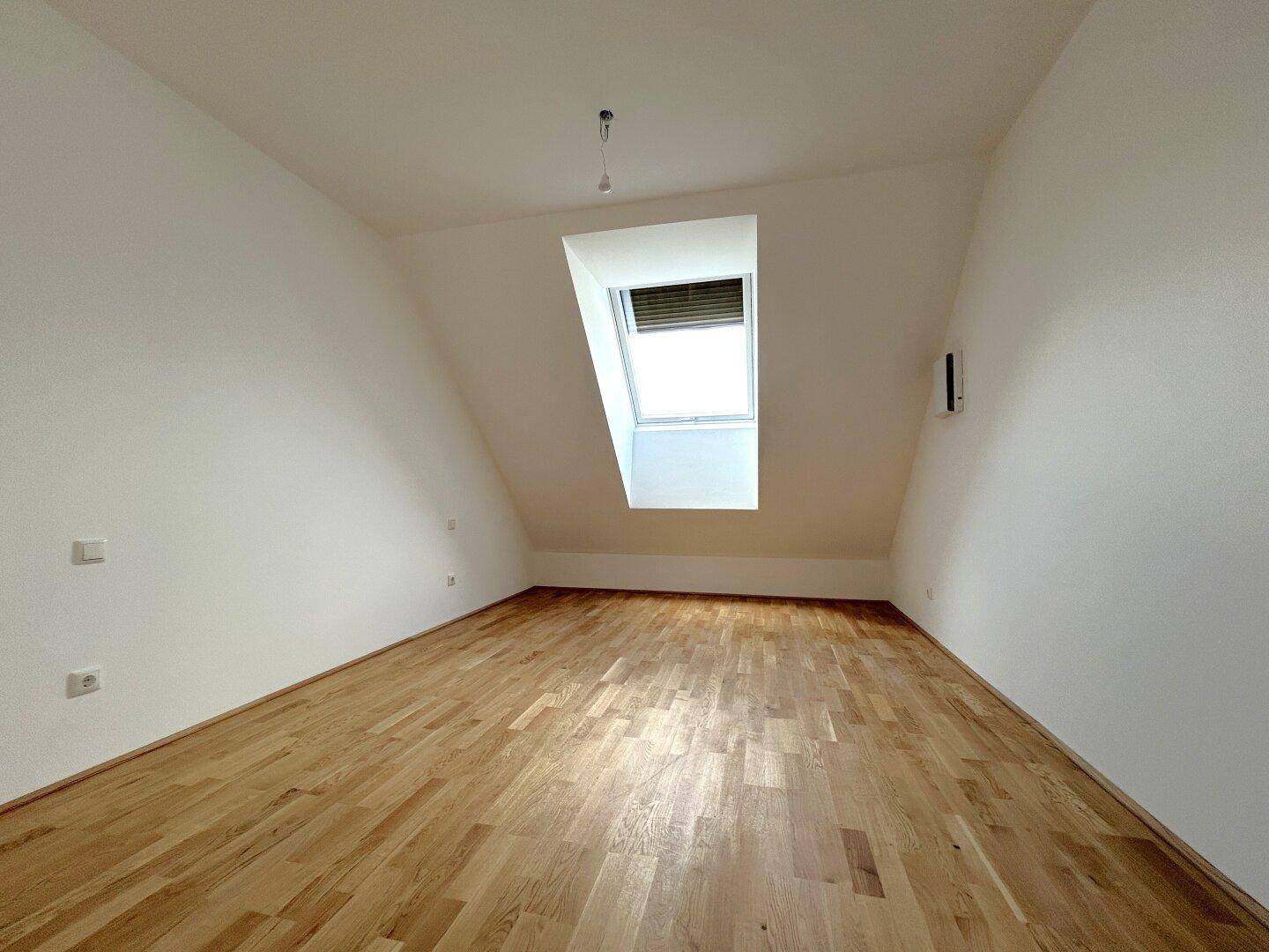 Heller Raum mit Holzboden und einem Dachfenster, das für natürliche Belichtung sorgt.