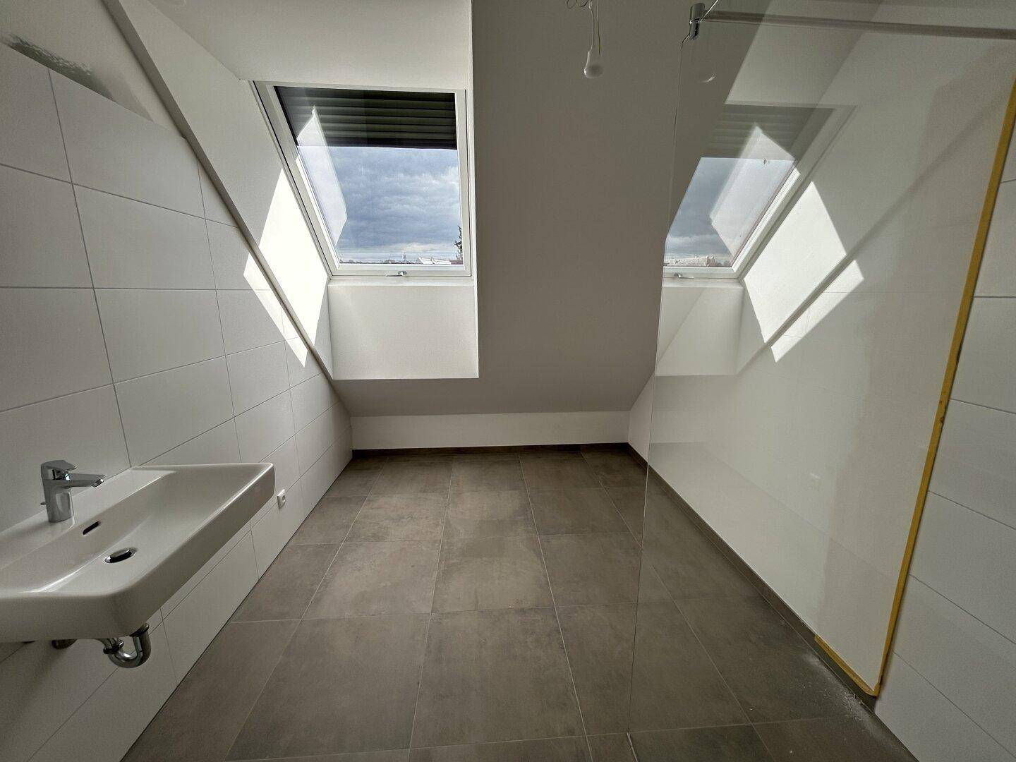 Modernes Badezimmer mit Waschbecken, Fliesenboden und zwei Dachfenstern für viel Licht.
