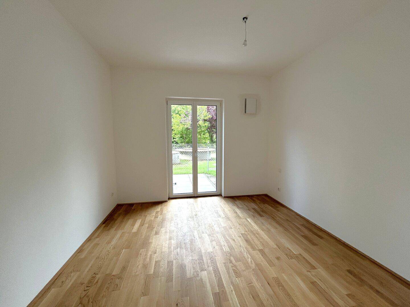 Freundliches Zimmer mit Holzboden und direktem Zugang zum grünen Außenbereich, perfekt für Ruhe.