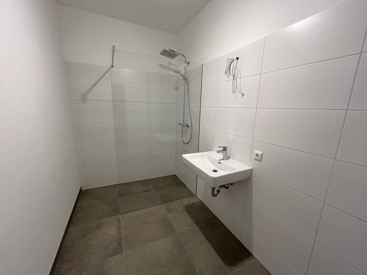 Modernes Badezimmer mit ebenerdiger Dusche, Wandwaschbecken und weißen Fliesen, funktional und hell.