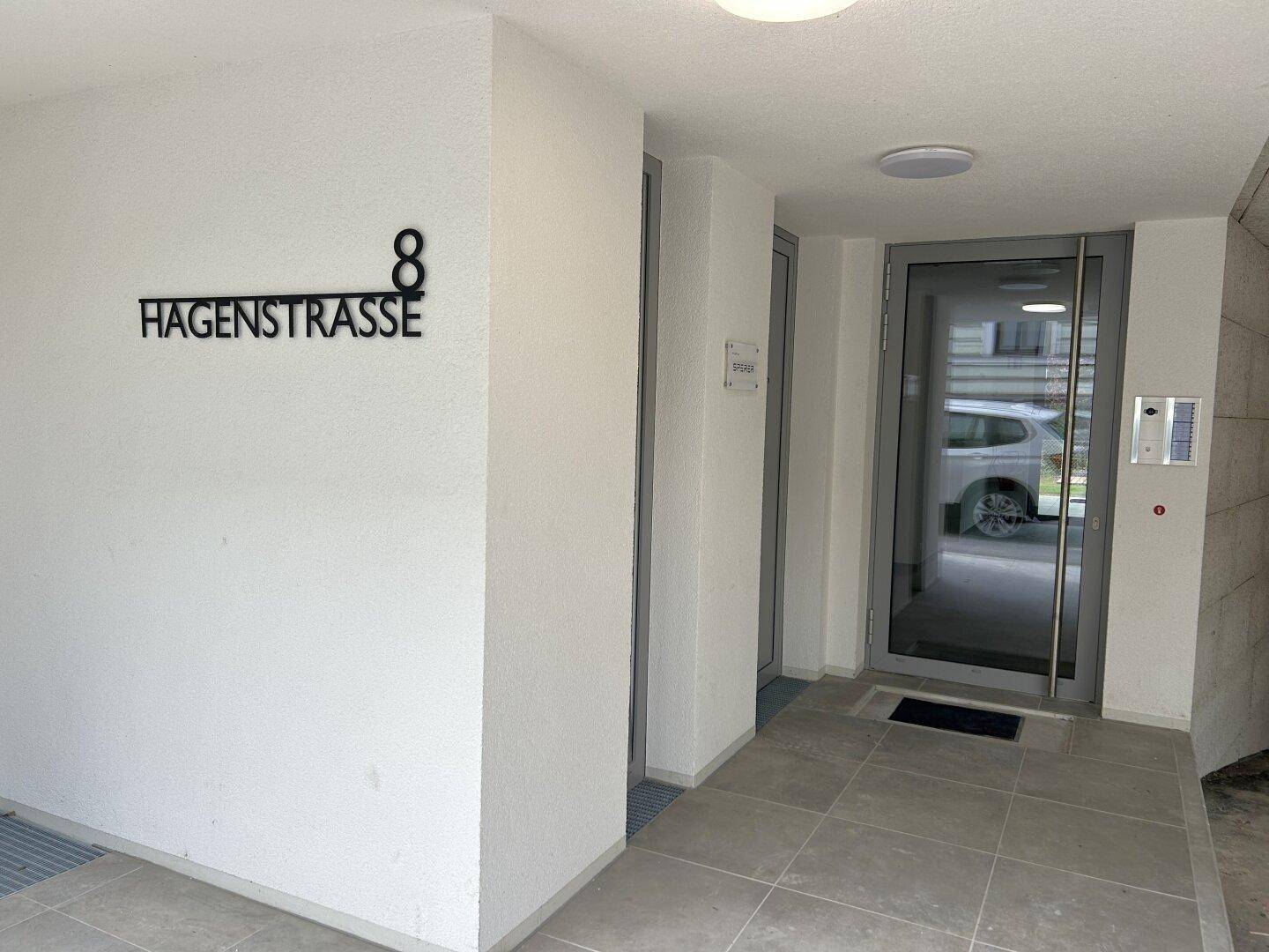 Moderner Eingangsbereich des Gebäudes mit Glasportal und Hausnummer 8 an der Hagenstrasse.