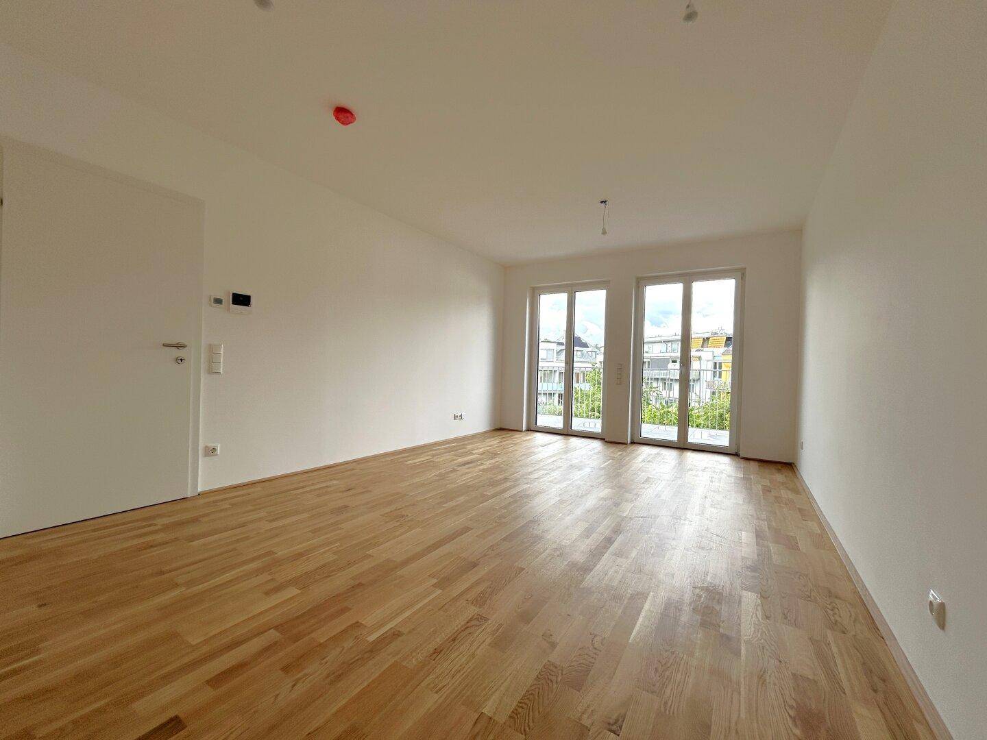 Lichtdurchfluteter Raum mit Holzboden und zwei Balkontüren, bereit für individuelle Gestaltung.