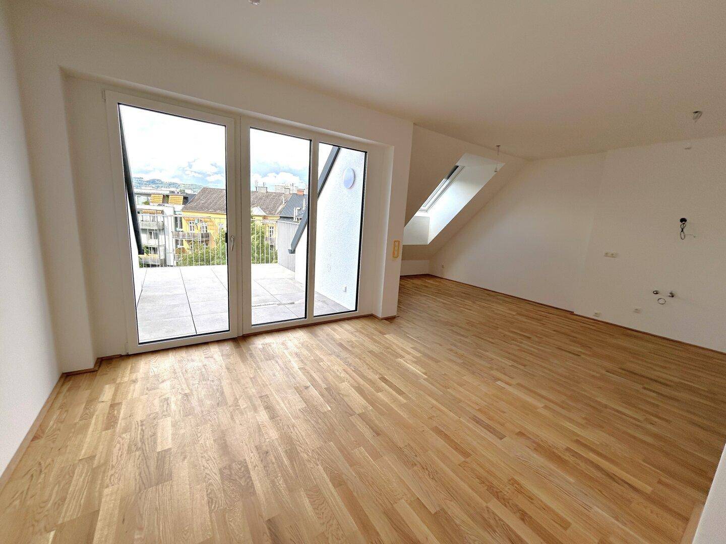 Helles Zimmer mit Holzboden, Zugang zu einer Terrasse und Dachfenster, ideal für Wohn- oder Schlafbereich.