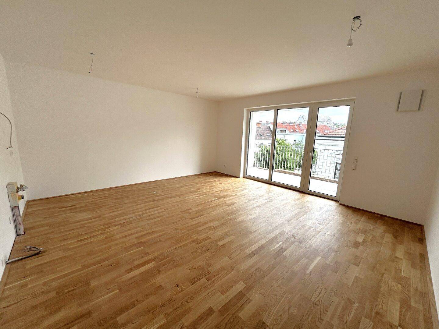 Heller Wohnraum mit Holzboden und breiter Glasfront, die zu einem Balkon führt.
