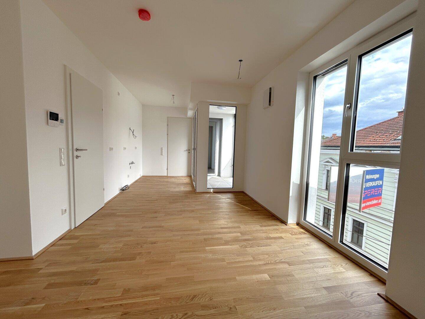 Heller Wohnbereich mit Holzboden und großen Fenstern, die einen Blick auf die Umgebung bieten.