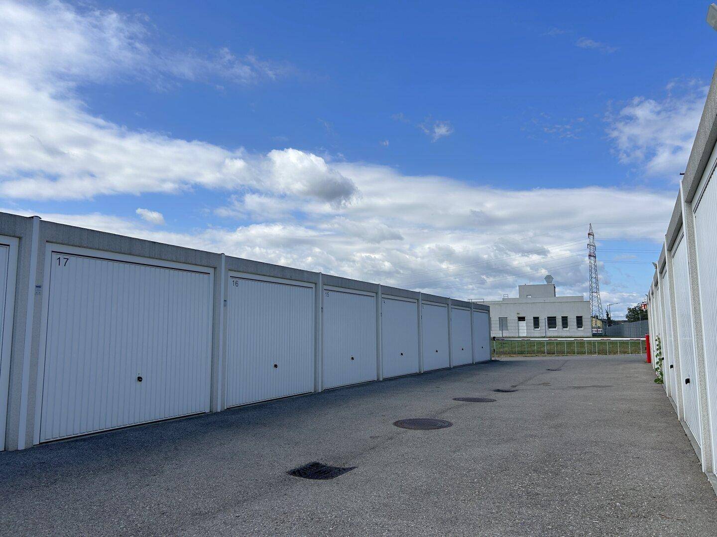 Reihe von Garagenboxen mit weißen Toren und Nummern, die sich unter einem weiten blauen Himmel erstrecken.