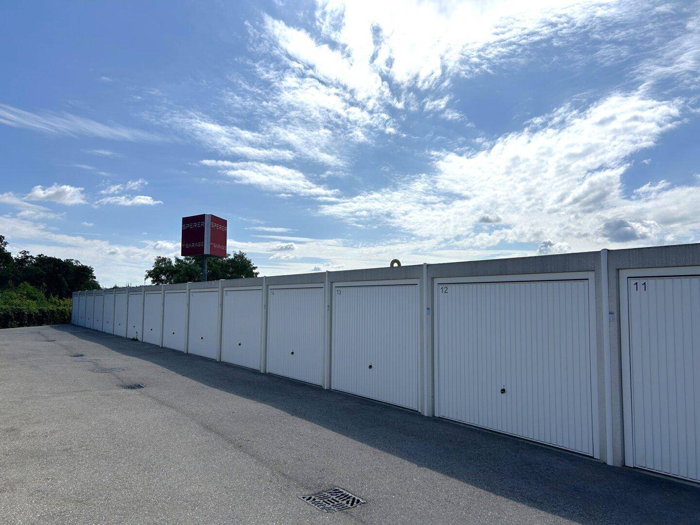 Lange Reihe von weißen Garagentoren unter einem bewölkten blauen Himmel, die individuelle Stellplätze bieten.