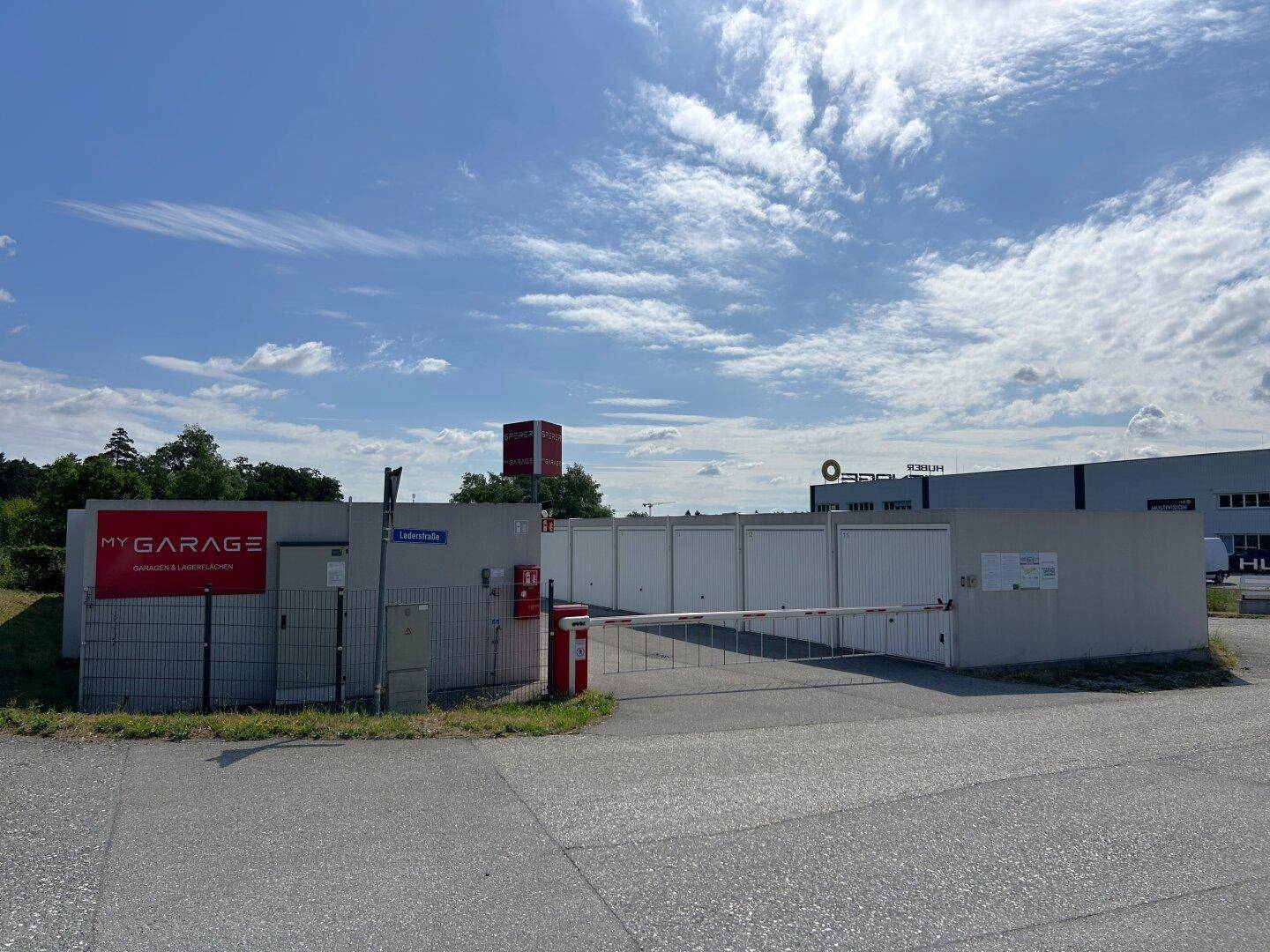 Übersicht des Garagenkomplexes mit Einfahrt, Schranke und Beschilderung unter einem sonnigen Himmel.