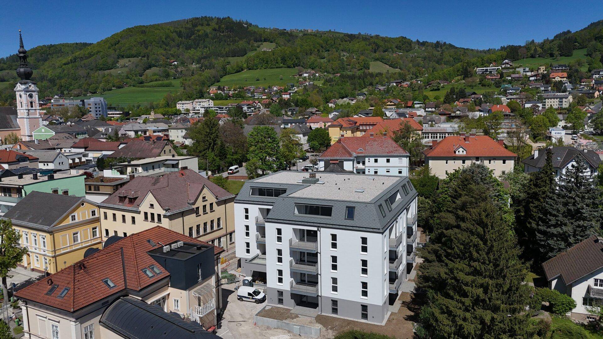 Luftaufnahme eines modernen Neubaus in einer städtischen Umgebung mit Bergblick.