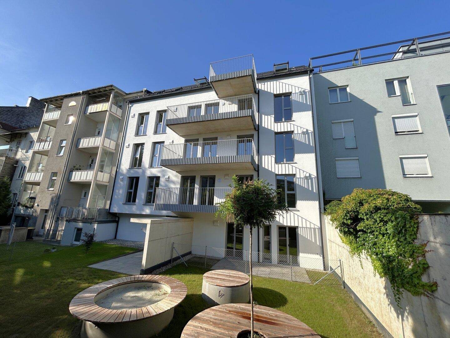 Moderne Wohnanlage mit Balkonen und einem gepflegten Gartenbereich mit Holzelementen.