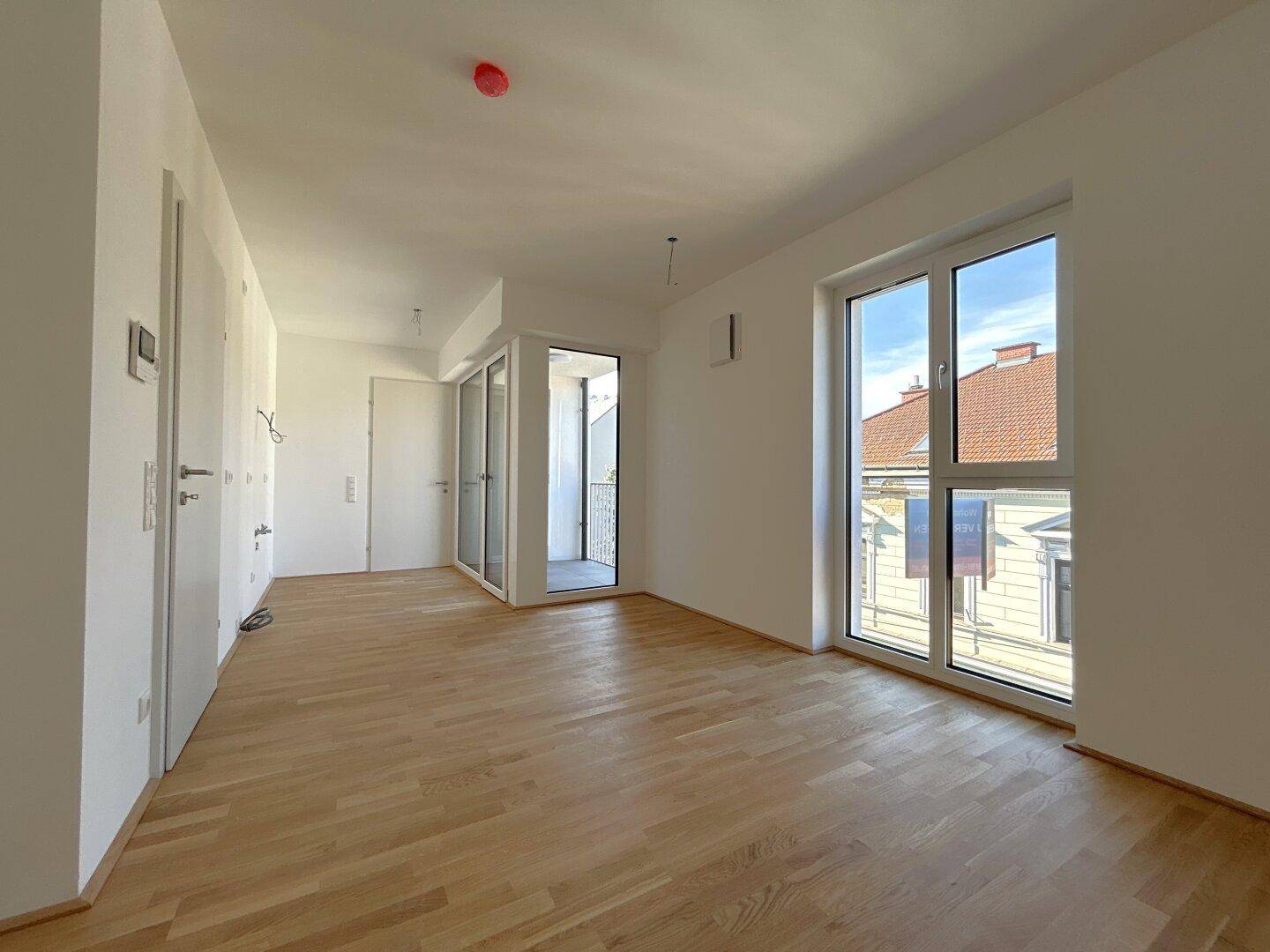 Geräumiger, heller Wohnraum mit Parkettboden und Zugang zu einem Balkon.