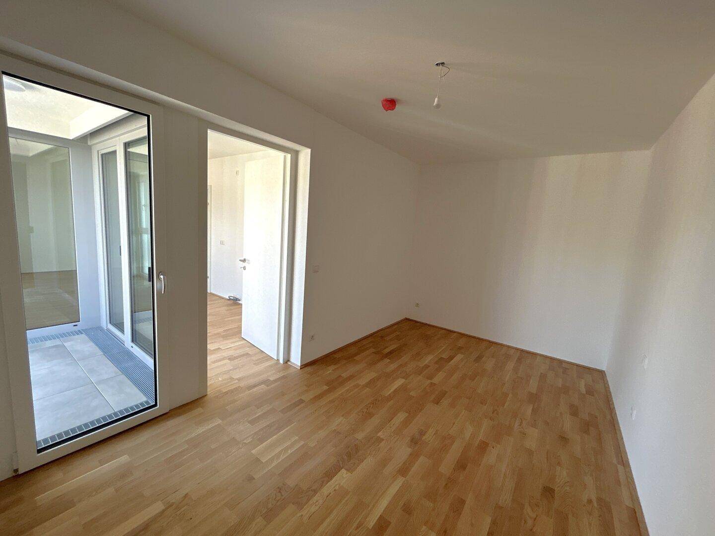 Lichtdurchfluteter Raum mit Holzparkett und breitem Zugang zu einem Außenbereich.
