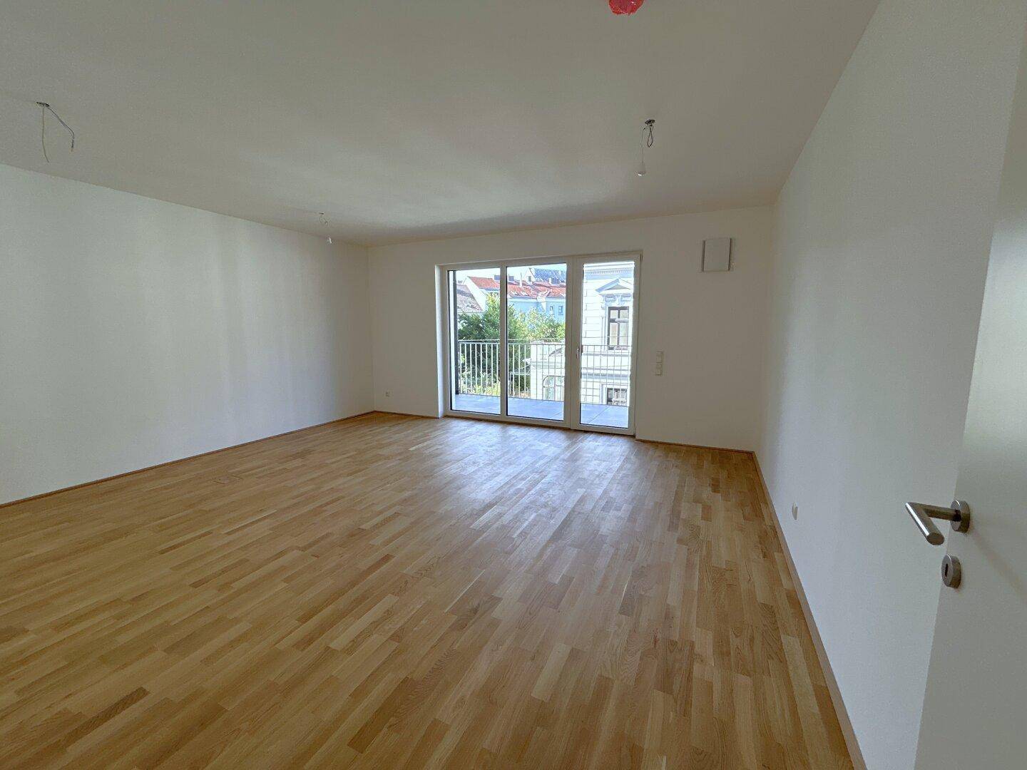 Geräumiges, helles Zimmer mit Parkettboden und Zugang zu einem französischen Balkon.