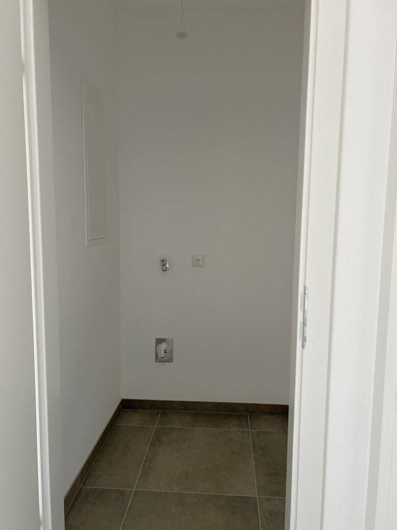 Praktischer Abstellraum mit Fliesenboden und Anschlüssen für Haushaltsgeräte und Waschmaschine.