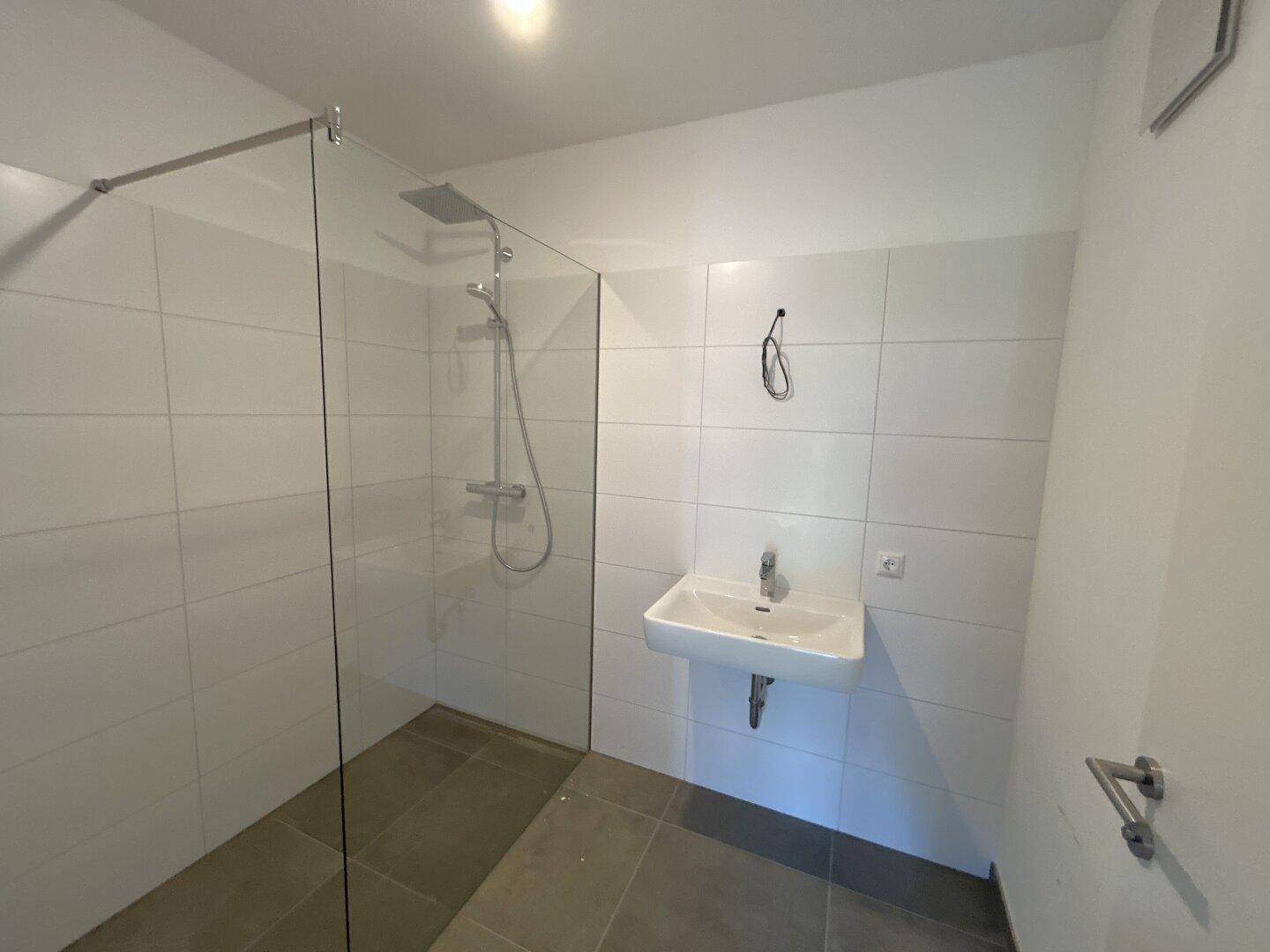 Modernes Badezimmer mit ebenerdiger Dusche, Waschbecken und weißen Fliesen an den Wänden.