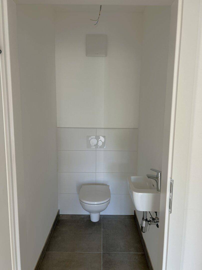 Kompaktes Gäste-WC mit wandhängender Toilette, kleinem Waschbecken und Fliesenboden.