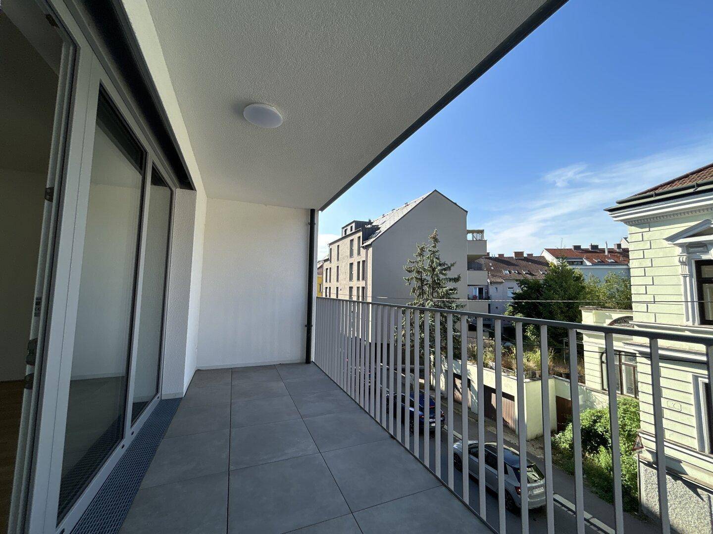Heller Balkon mit Fliesenboden und Metallgeländer, bietet einen Blick auf die umliegende Nachbarschaft.