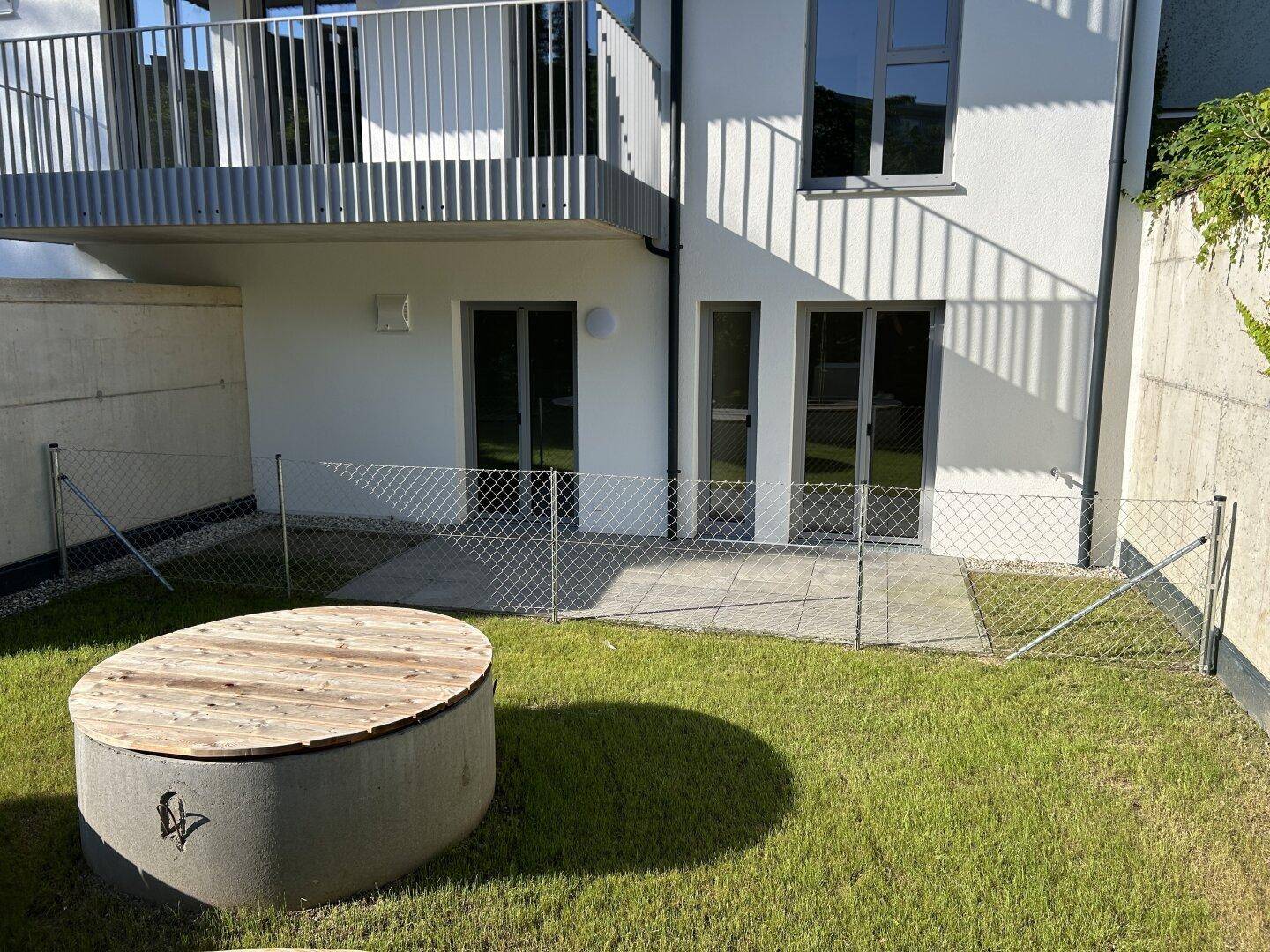 Gepflegter Gartenbereich mit Rasen, Terrasse und einem runden Hochbeet vor der Gebäudefassade.
