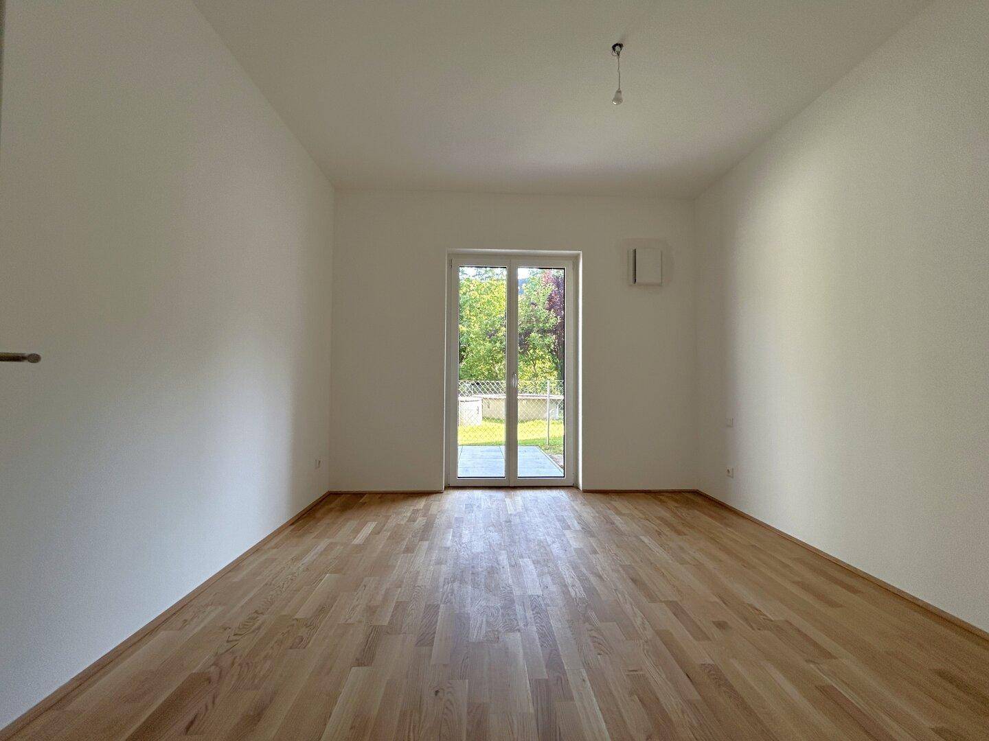 Helles Schlafzimmer mit Holzboden und Fenstertür, die direkten Zugang zum Garten bietet.