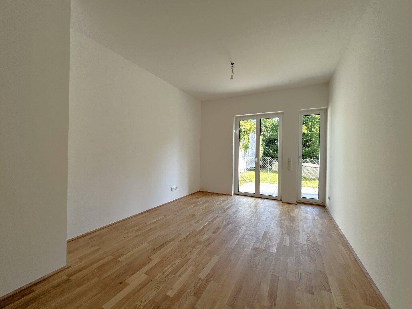 Helles, leeres Zimmer mit Eichenparkettboden und großen Fenstertüren zum Garten.