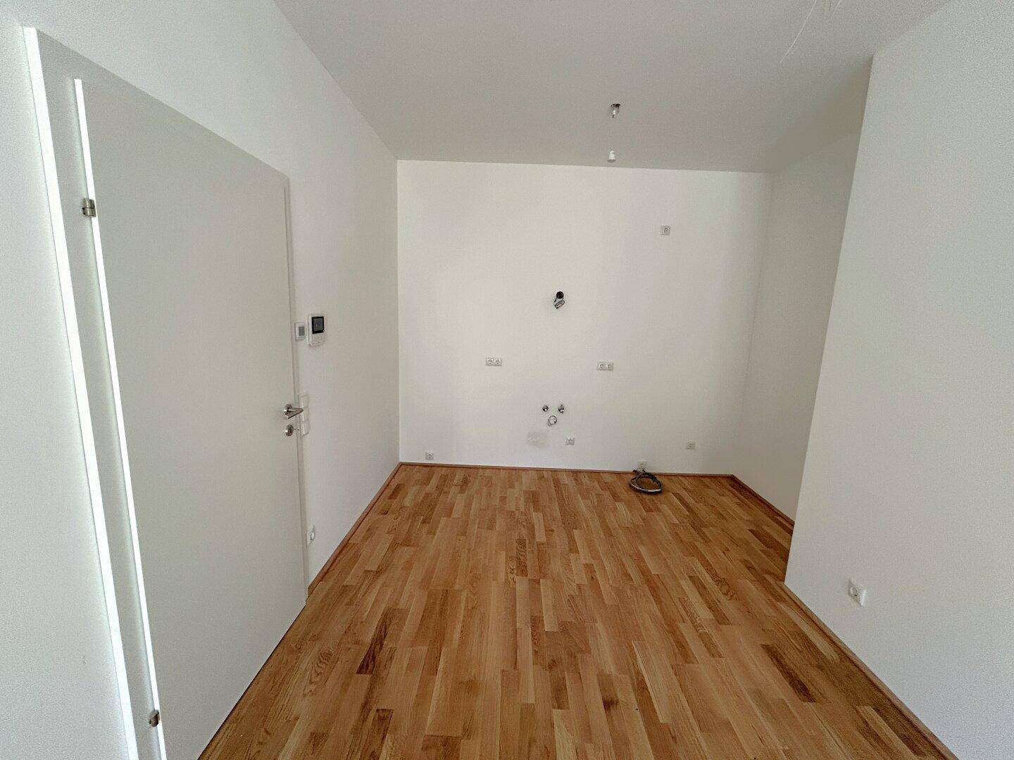 Leerer Raum mit Holzboden und Anschlüssen für eine zukünftige Küche oder Hauswirtschaftsraum.
