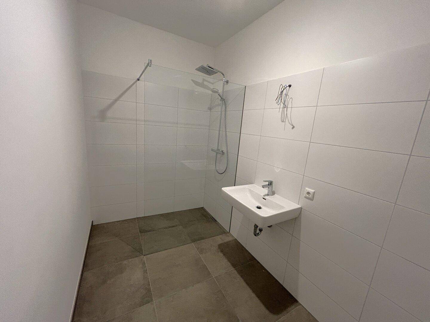 Modernes Badezimmer mit weißen Fliesen, ebenerdiger Dusche und wandhängendem Waschbecken.