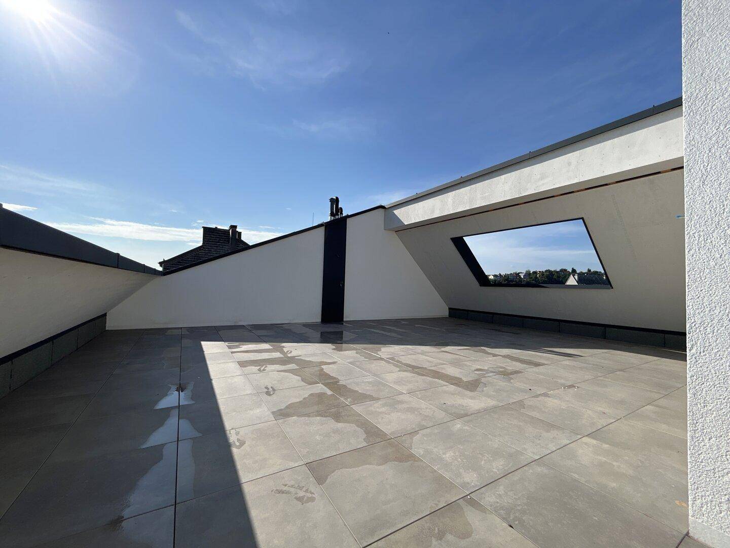 Geräumige Dachterrasse mit Fliesenboden und viel Sonnenlicht unter blauem Himmel.