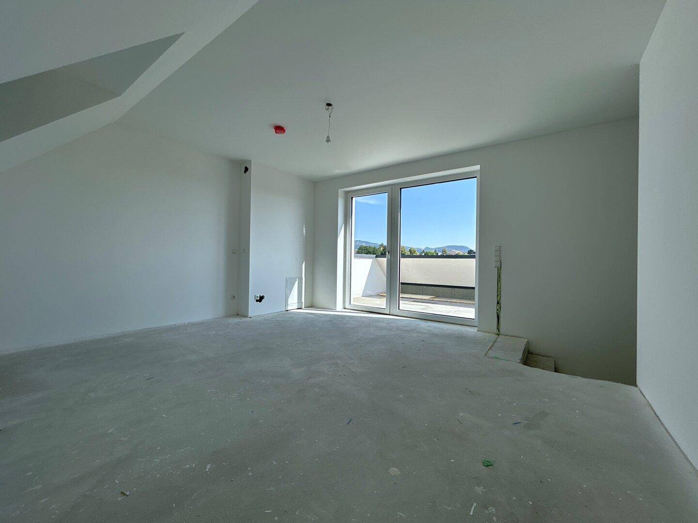 Unfertiger Raum mit Betonboden und großen Fenstern, bereit für den Innenausbau.