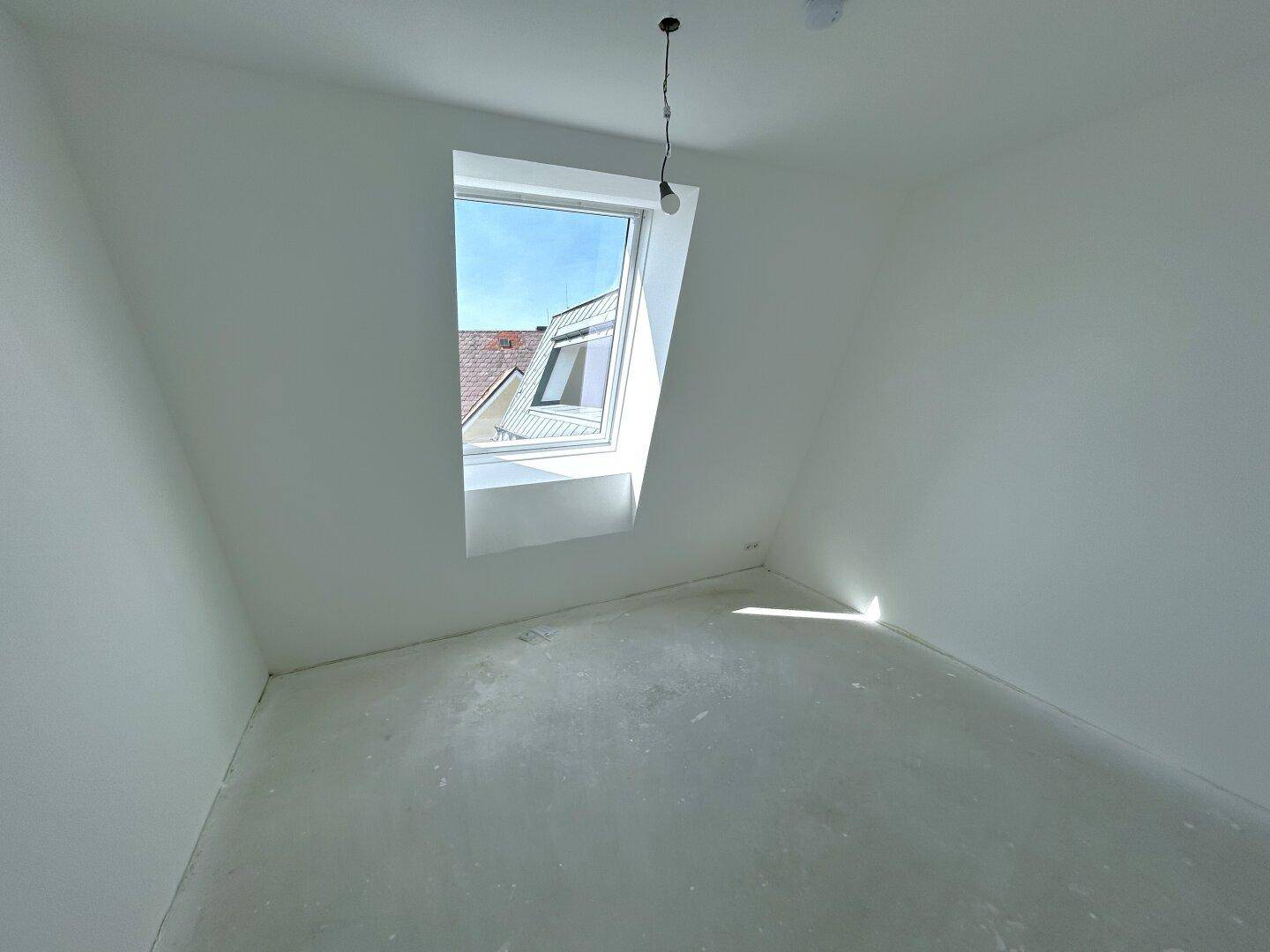 Dachgeschosszimmer mit schrägen Wänden und einem großen Dachfenster für viel Tageslicht.