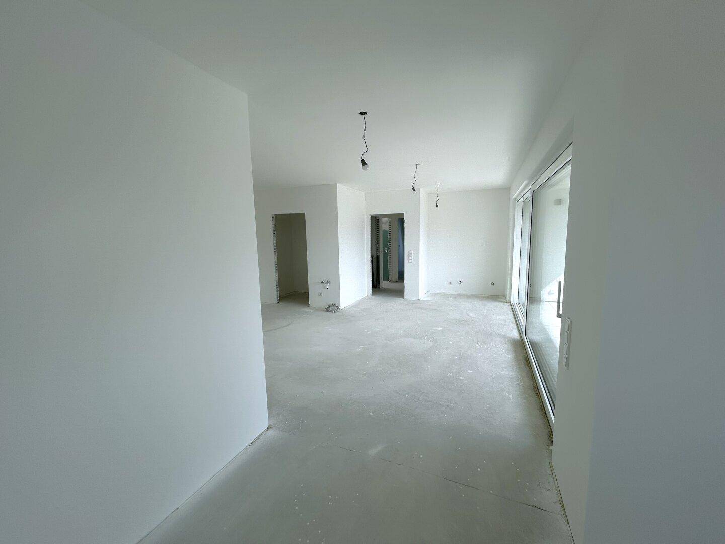 Unfertiger Innenraum mit weißen Wänden und Rohbetonboden, bereit für den Ausbau.