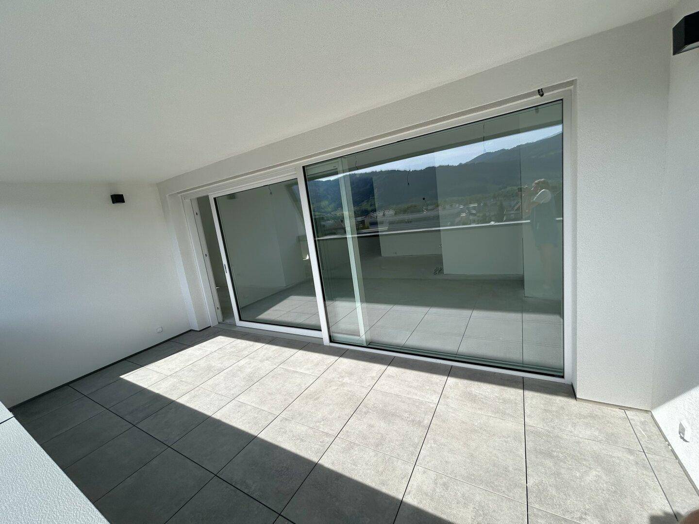 Heller Balkon mit großen Schiebetüren und Blick auf die grüne Umgebung.
