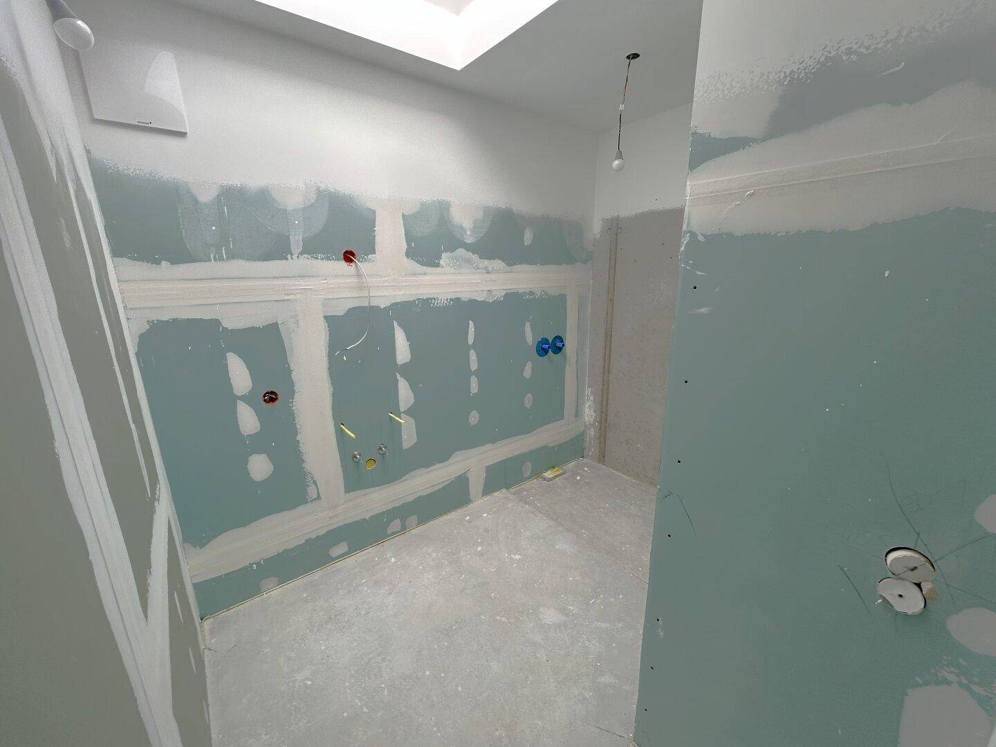Unfertiges Badezimmer mit vorbereiteten Installationen und einer Deckenluke für Licht.