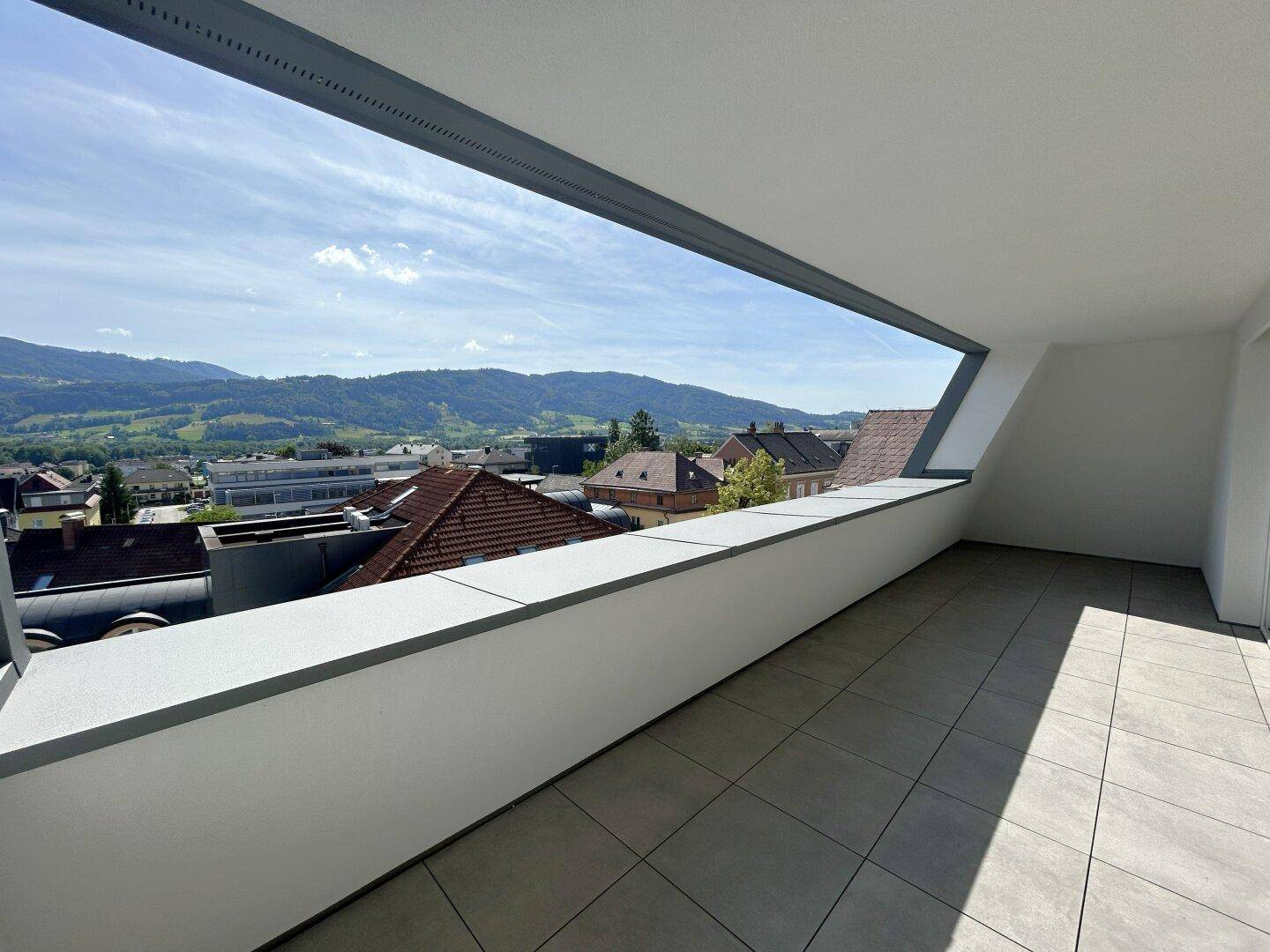 Heller Balkon mit Fliesenboden und einer beeindruckenden Panoramaaussicht auf die umliegende Landschaft und Berge.