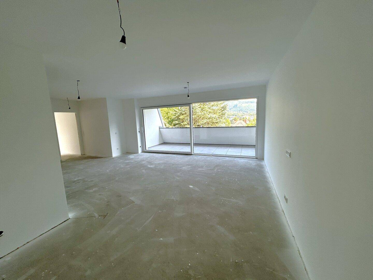 Heller, unmöblierter Wohnbereich im Rohbau mit großen Schiebetüren zum Balkon und viel Tageslicht.