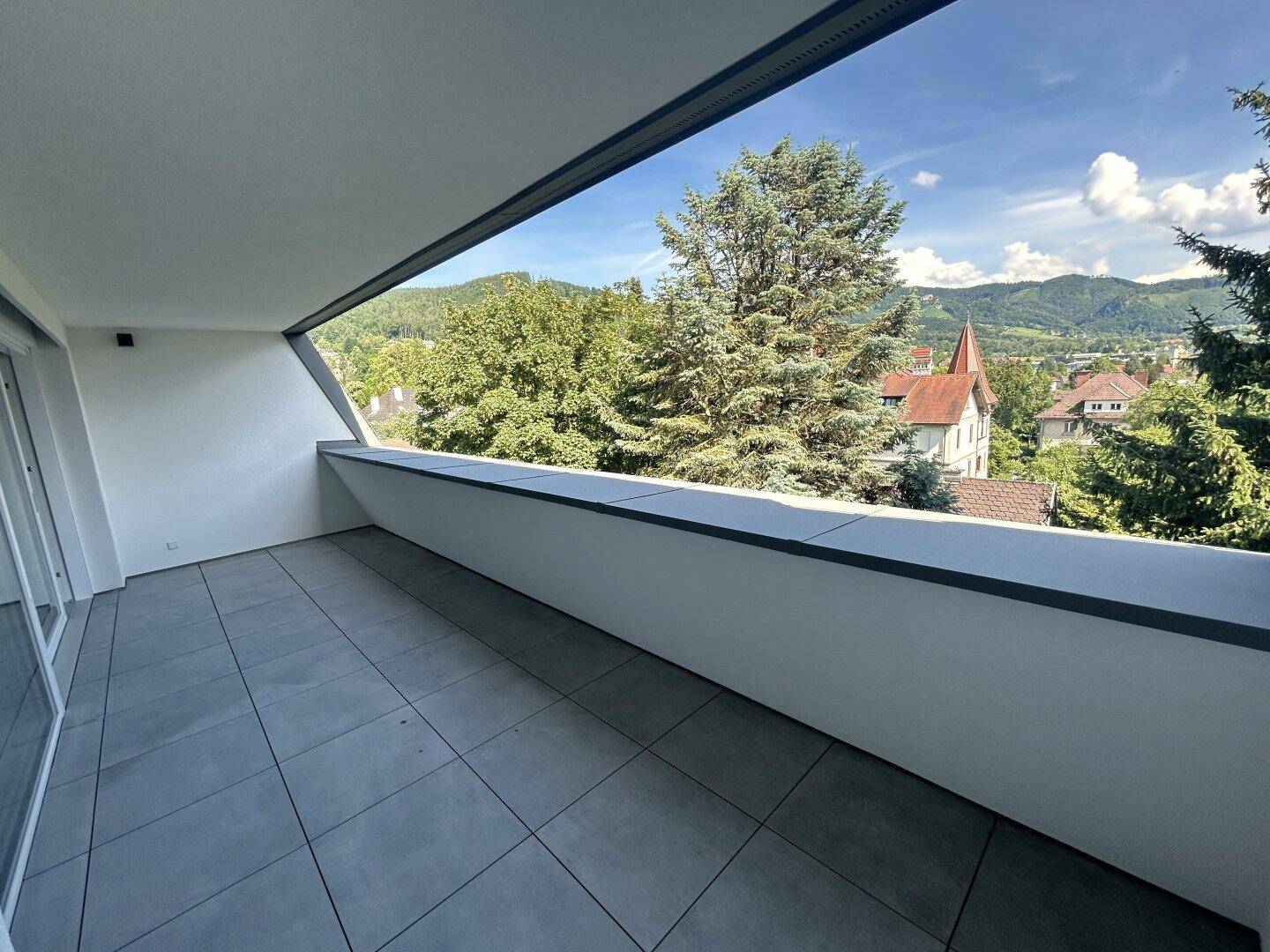 Heller Balkon mit moderner Gestaltung und Panoramablick über die grüne Umgebung und die Berge.