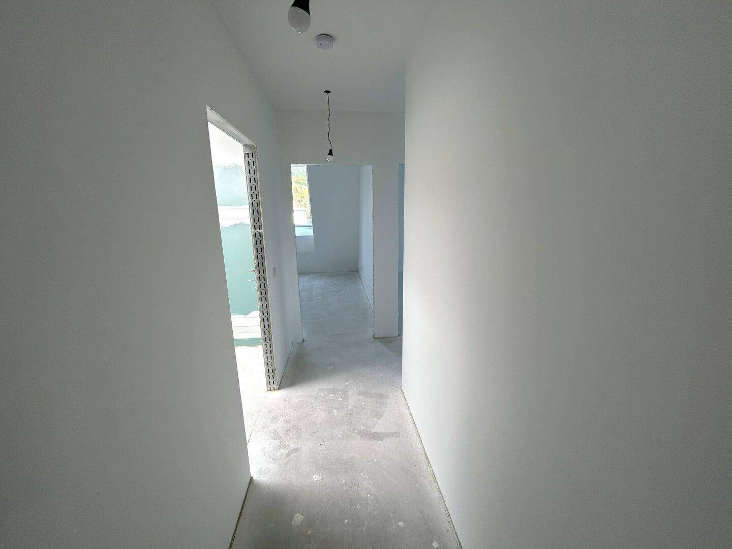 Unfertiger Flur im Rohbau mit glatten weißen Wänden und Betonboden, bereit für den Ausbau.