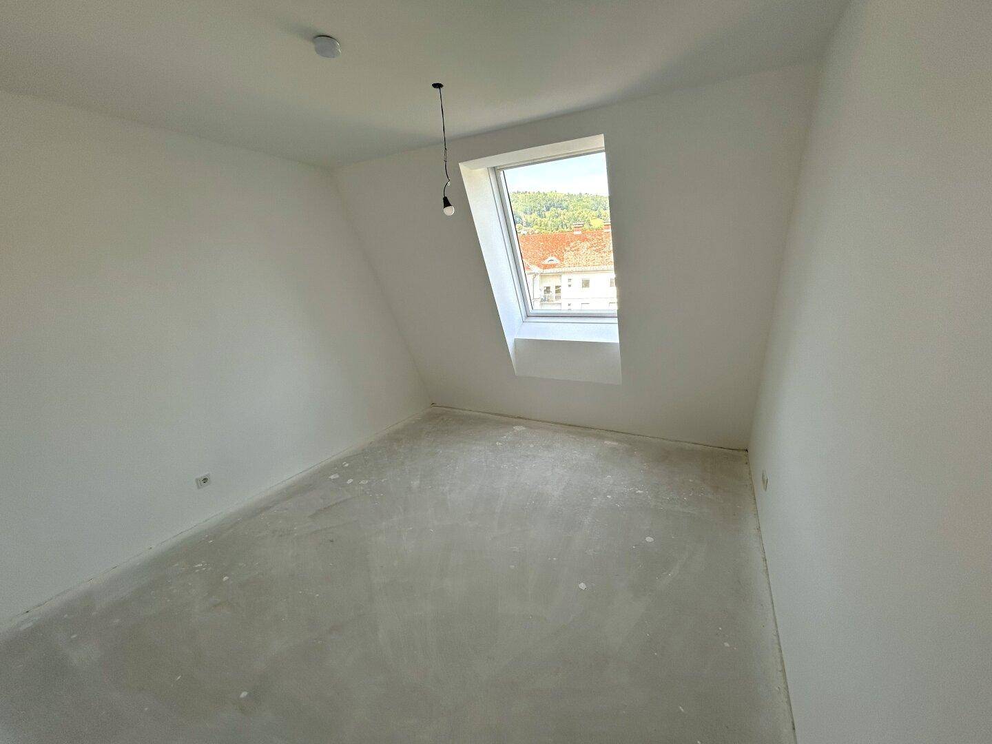 Unmöbliertes Schlafzimmer im Dachgeschoss mit einem großen Dachfenster und Blick auf die Umgebung.