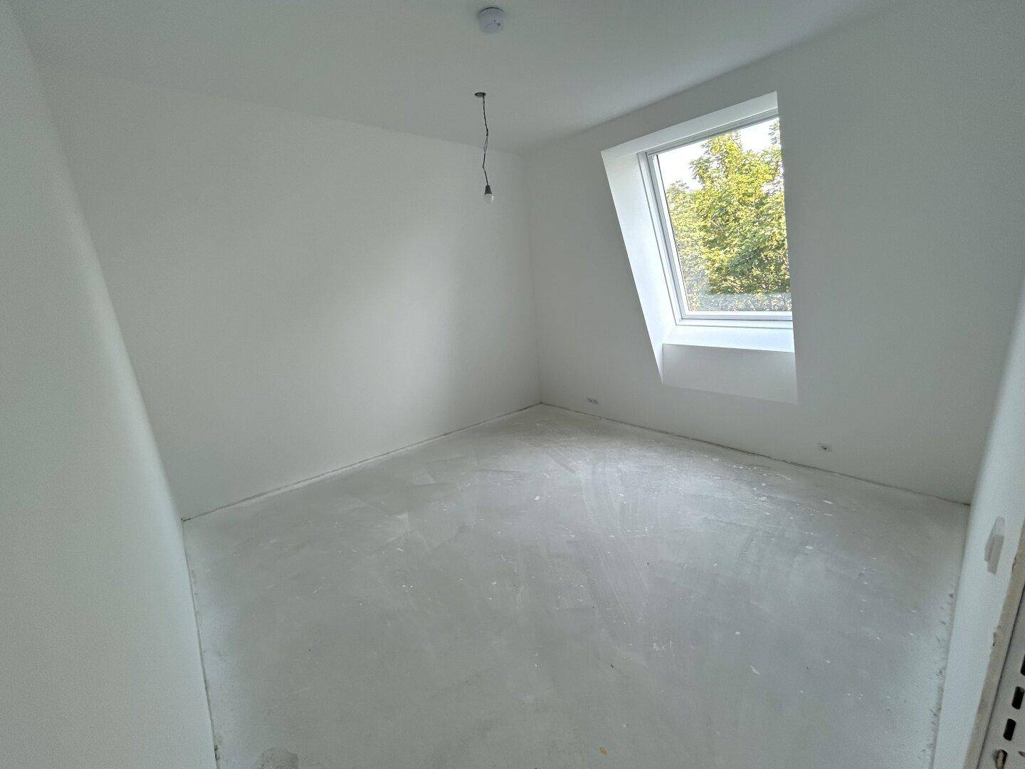 Geräumiges Schlafzimmer im Rohbau mit Dachschräge und großem Dachfenster, das viel Licht hereinlässt.