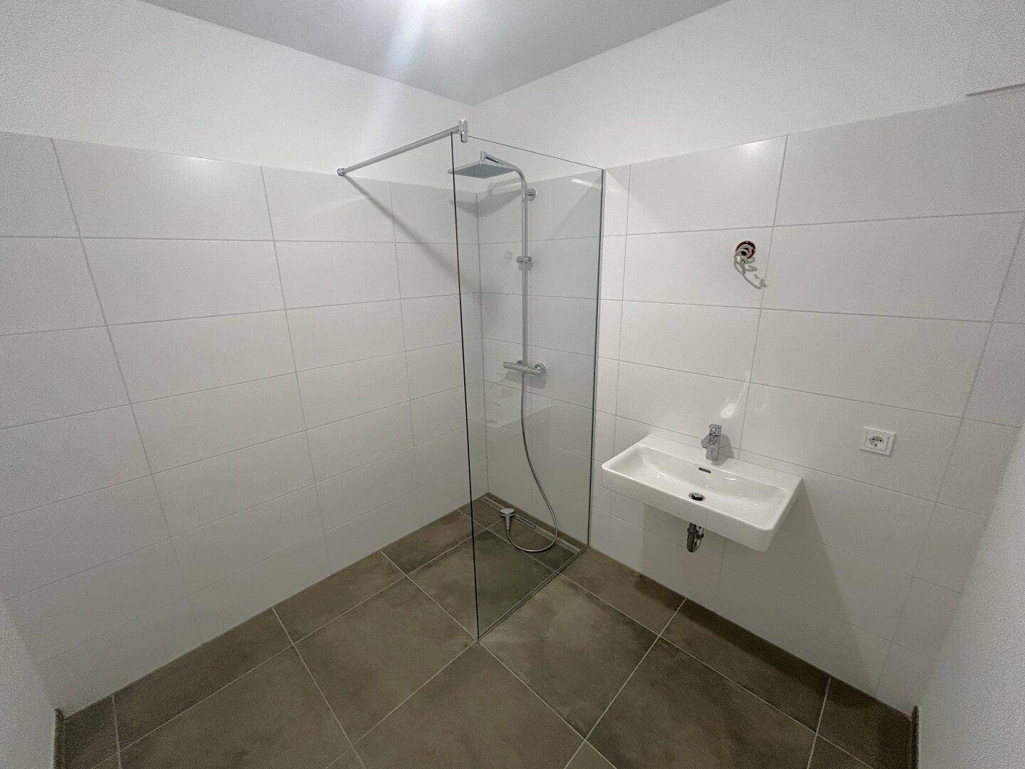 Modernes Badezimmer mit ebenerdiger Dusche, Fliesenboden und weißem Waschbecken.