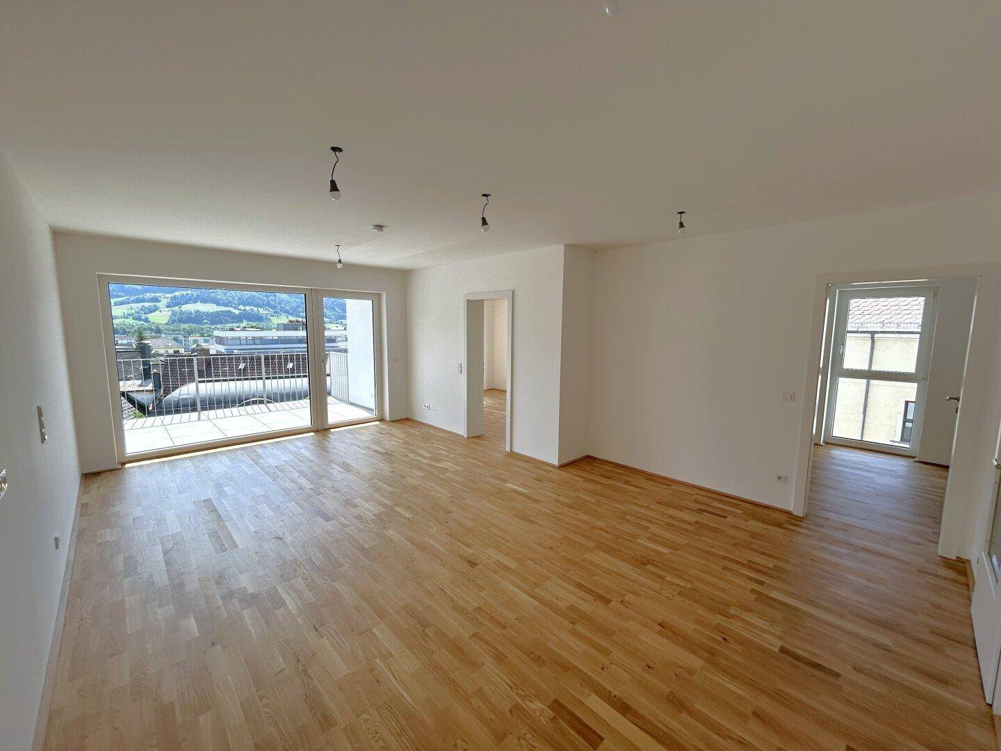 Großzügiger, heller Wohnbereich mit hochwertigem Parkettboden und Zugang zum Balkon.
