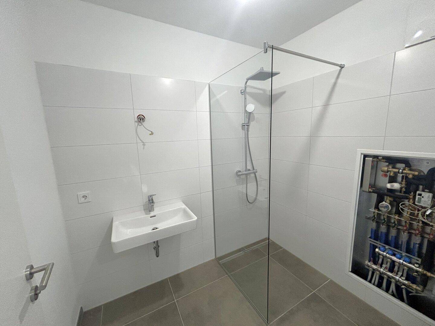 Modernes Badezimmer mit weiß gefliesten Wänden, begehbarer Dusche und wandhängendem Waschbecken.
