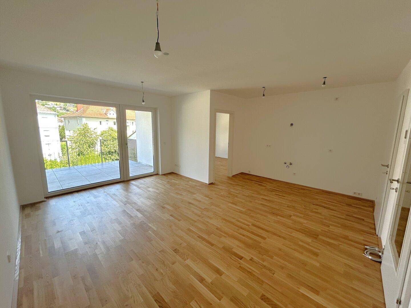 Geräumiges Wohnzimmer mit hellem Parkettboden und direktem Zugang zu einem sonnigen Balkon.