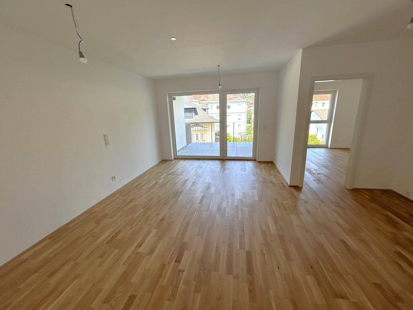 Geräumiges Wohnzimmer mit Parkettboden und großen Fenstern, die viel Tageslicht hereinlassen.