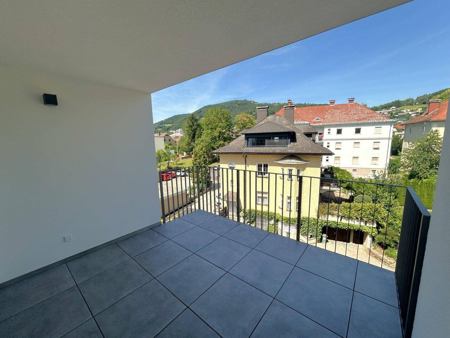 Balkon mit Fliesenboden und Blick auf die umliegende Wohngegend und grüne Hügel.