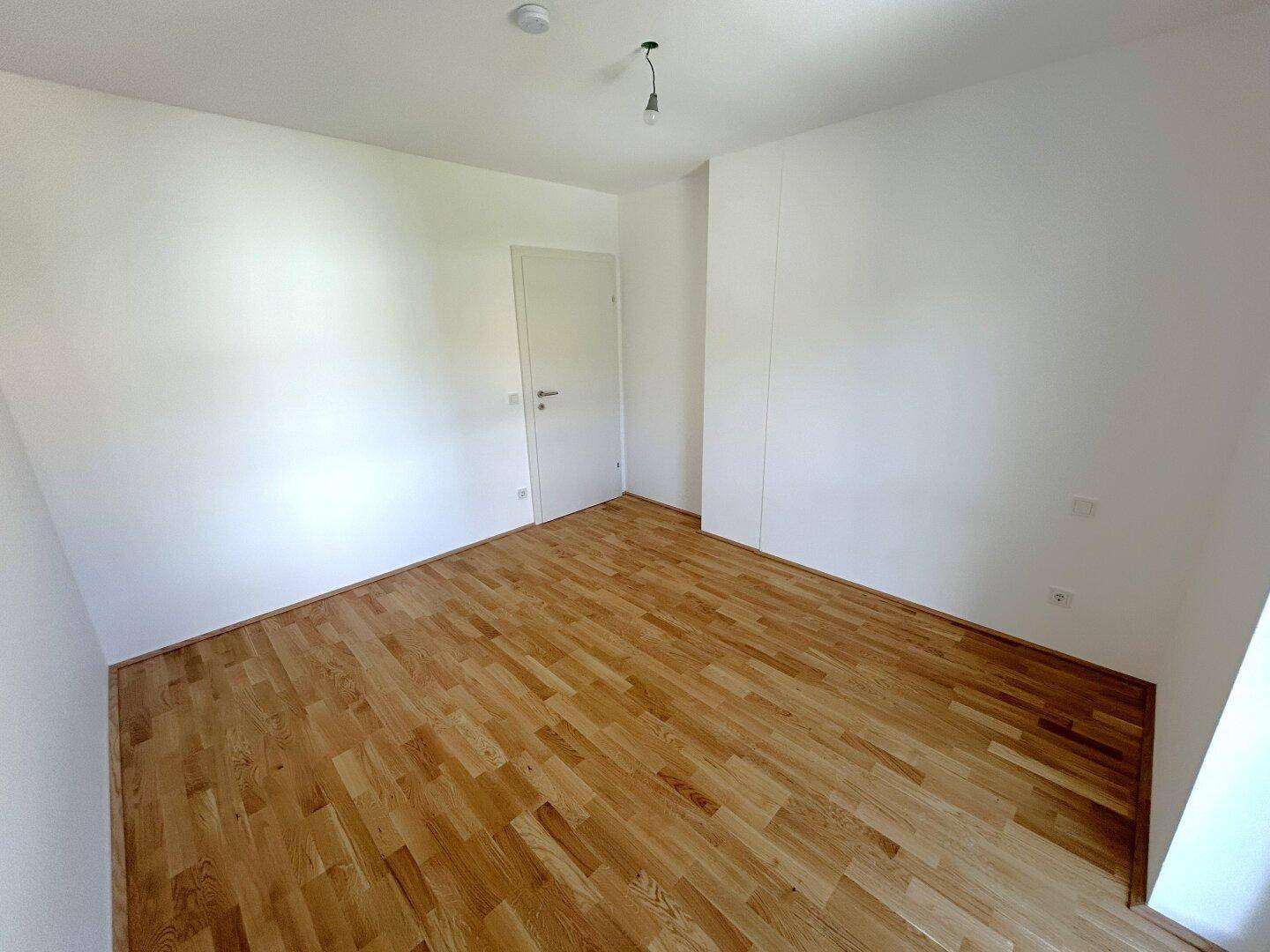 Leeres Zimmer mit neuem Holzboden und weißen Wänden, ideal als Schlaf- oder Arbeitszimmer.