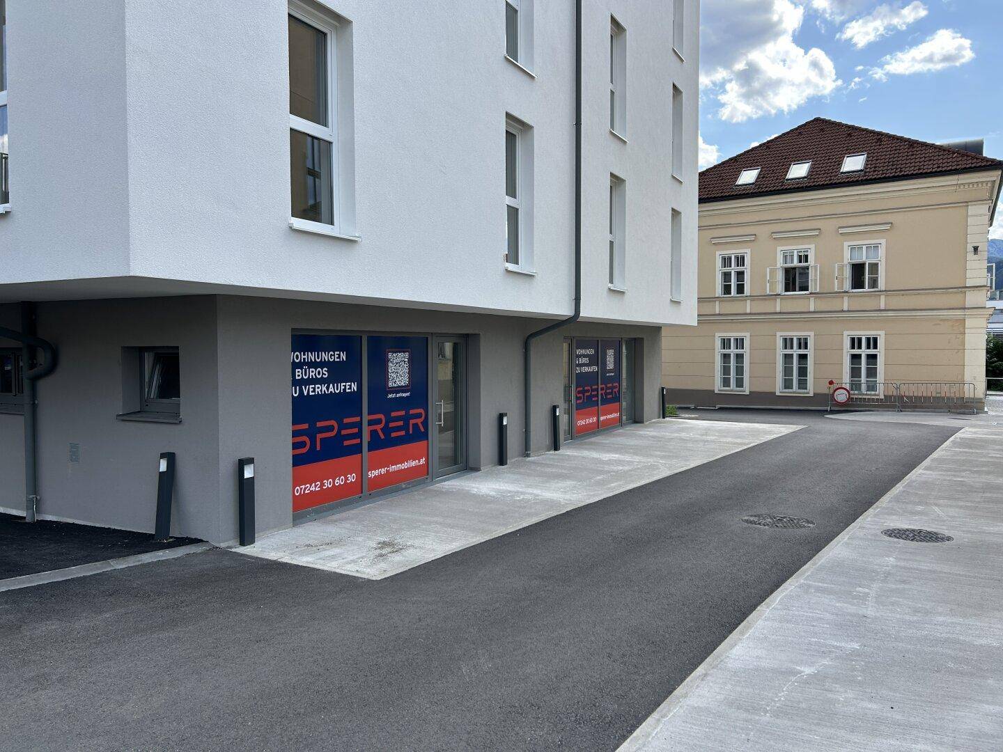 Nahaufnahme der Geschäftsflächen im Erdgeschoss des modernen Gebäudes mit Werbeplakaten.