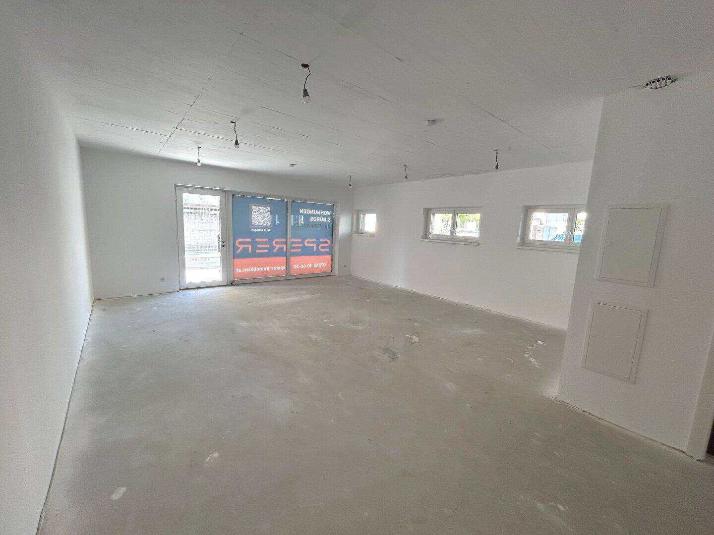 Unfertiger Gewerberaum mit Betonboden und weißen Wänden, bereit für den Ausbau.