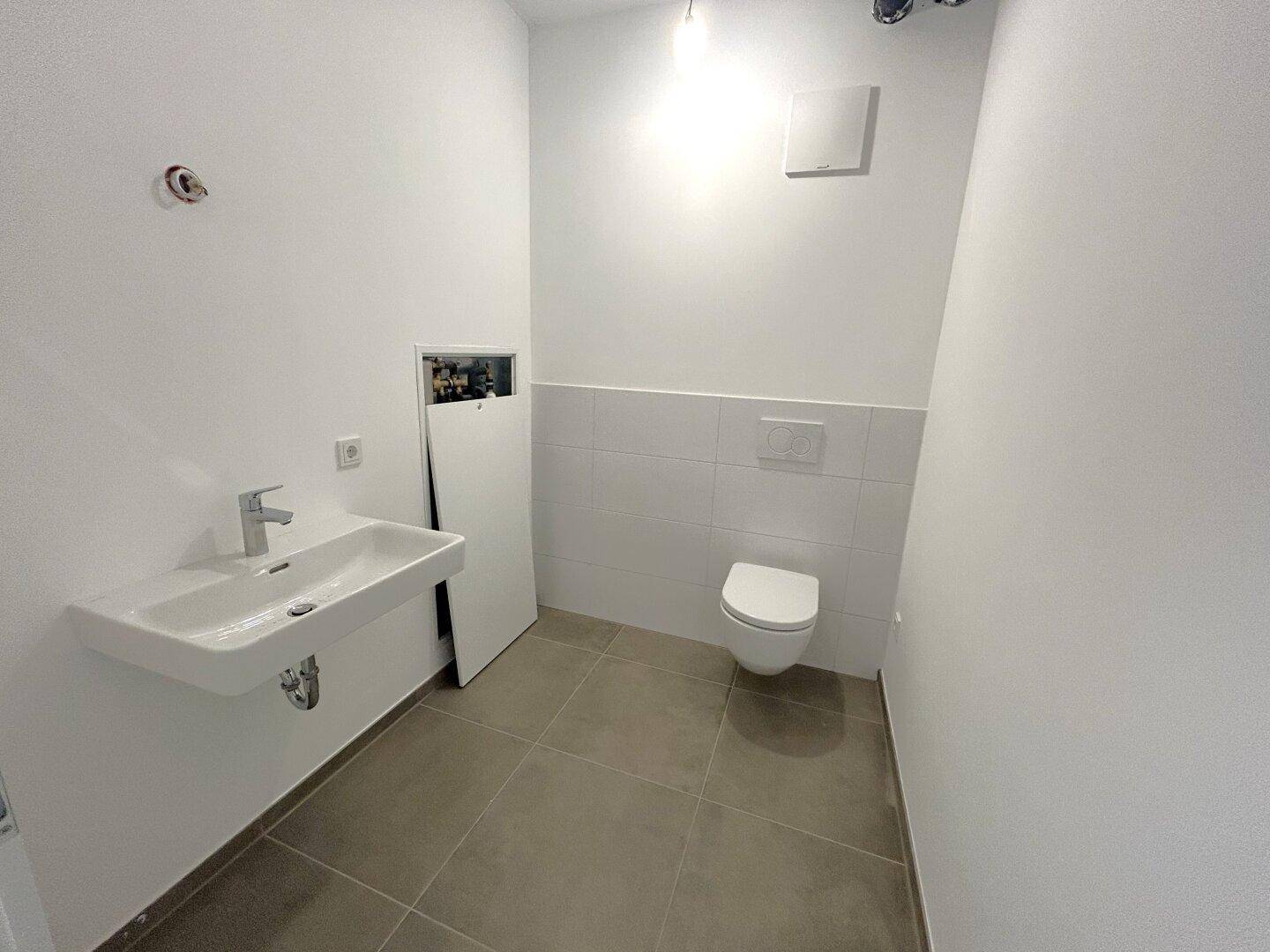 Modernes Gäste-WC mit wandhängender Toilette, Waschbecken und grauen Bodenfliesen.